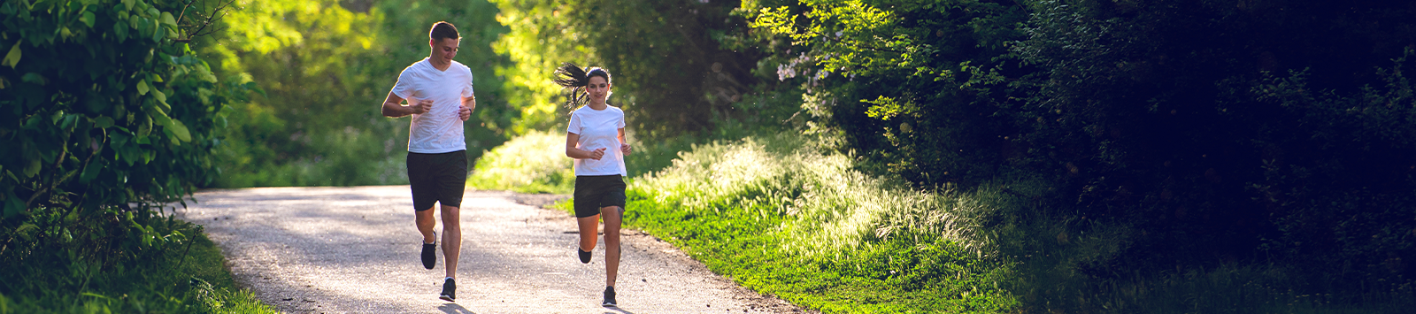 A man and a woman job down a dirt path surrounded by lush forestation