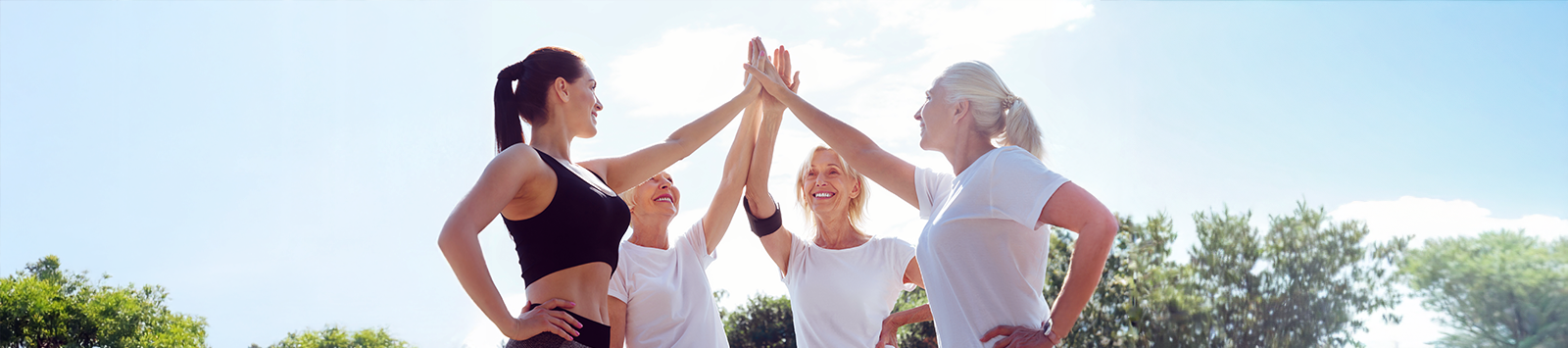 Four women of varying ages, wearing workout gear, high-five.